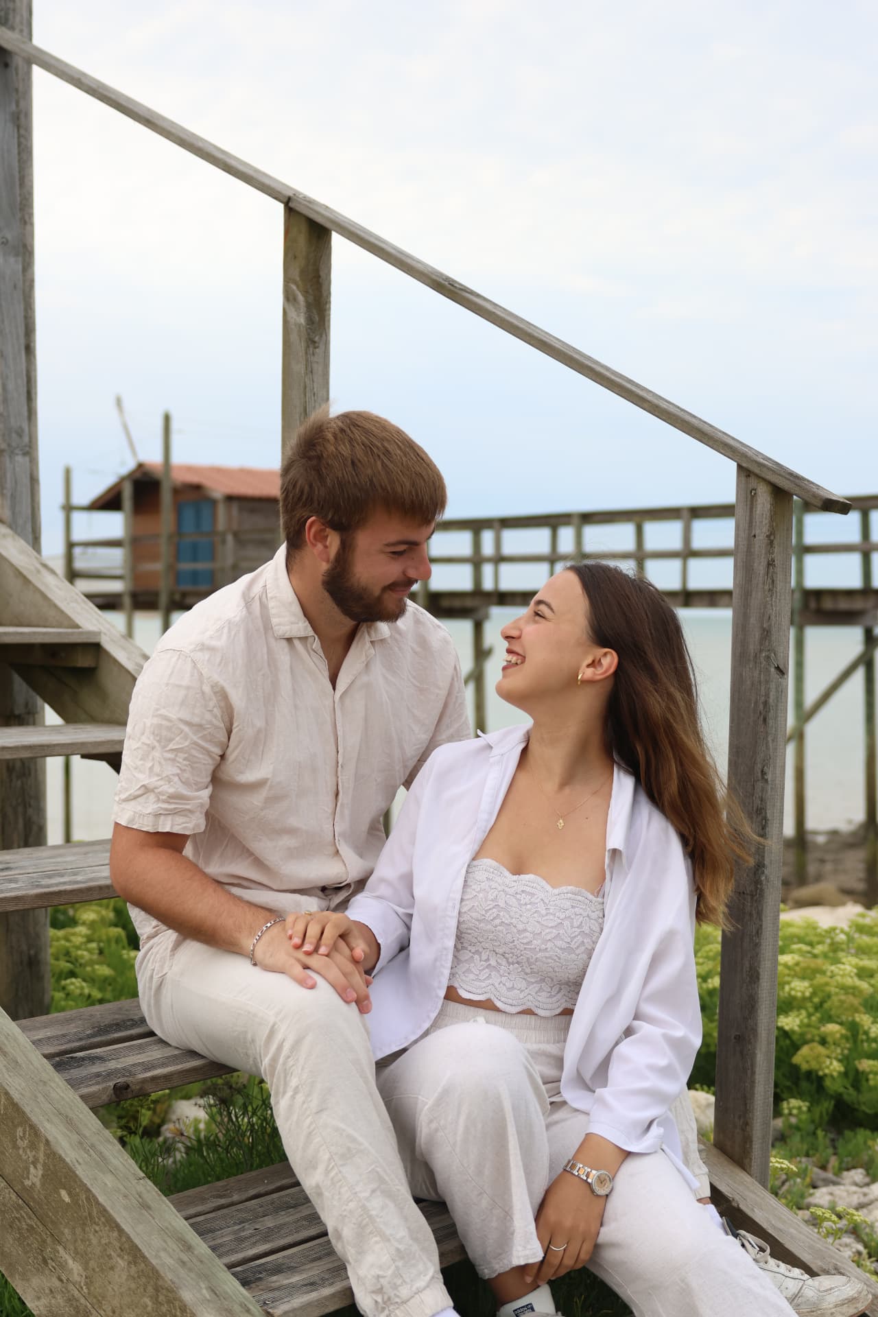 Couple assis sur les marches en bois d'un accès plage, complices