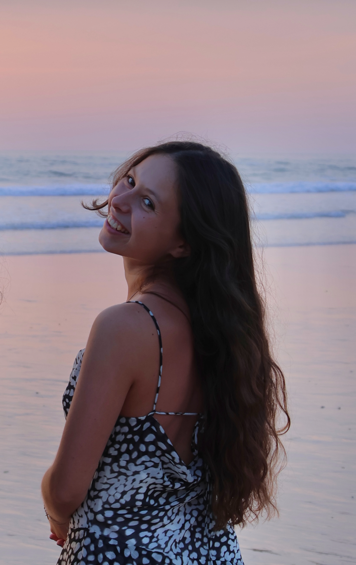 Jeune femme en robe à motifs, de dos, se retournant et souriant sur la plage au crépuscule