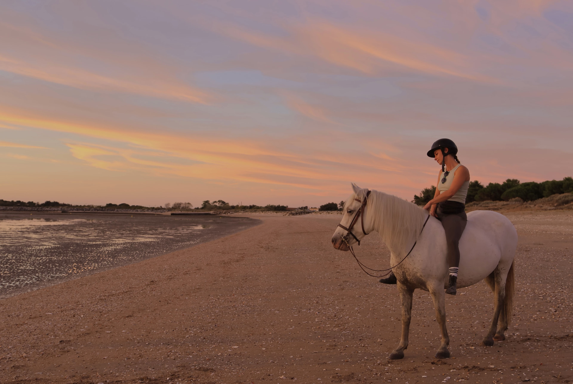 Cavalière casquée sur son cheval blanc sur la plage au coucher du soleil près de La Rochelle